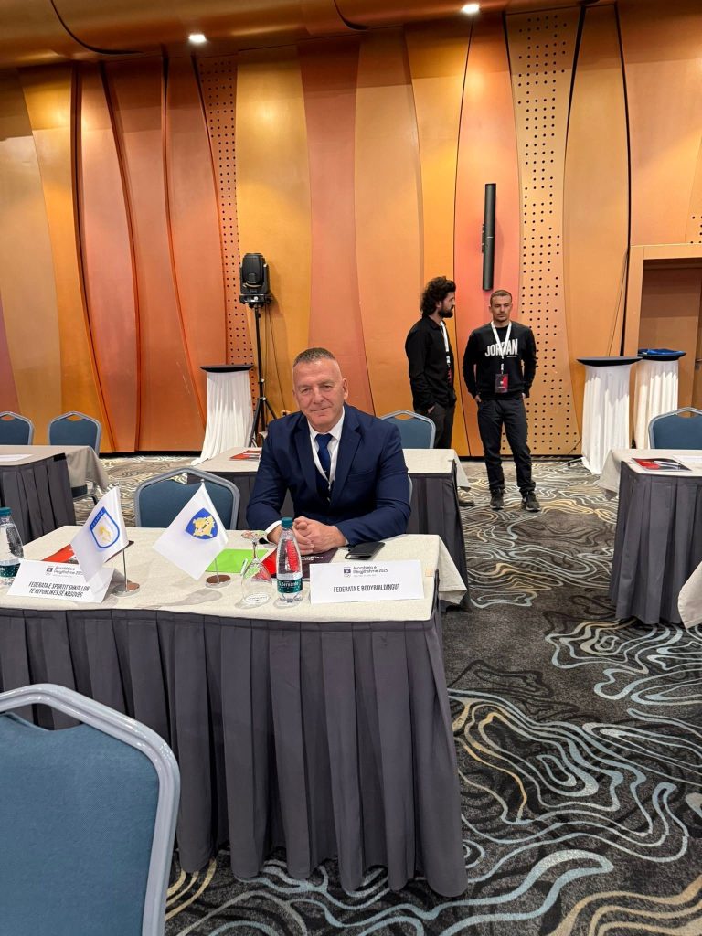 Një burrë i ulur në tryezë në sallën e asamblesë.