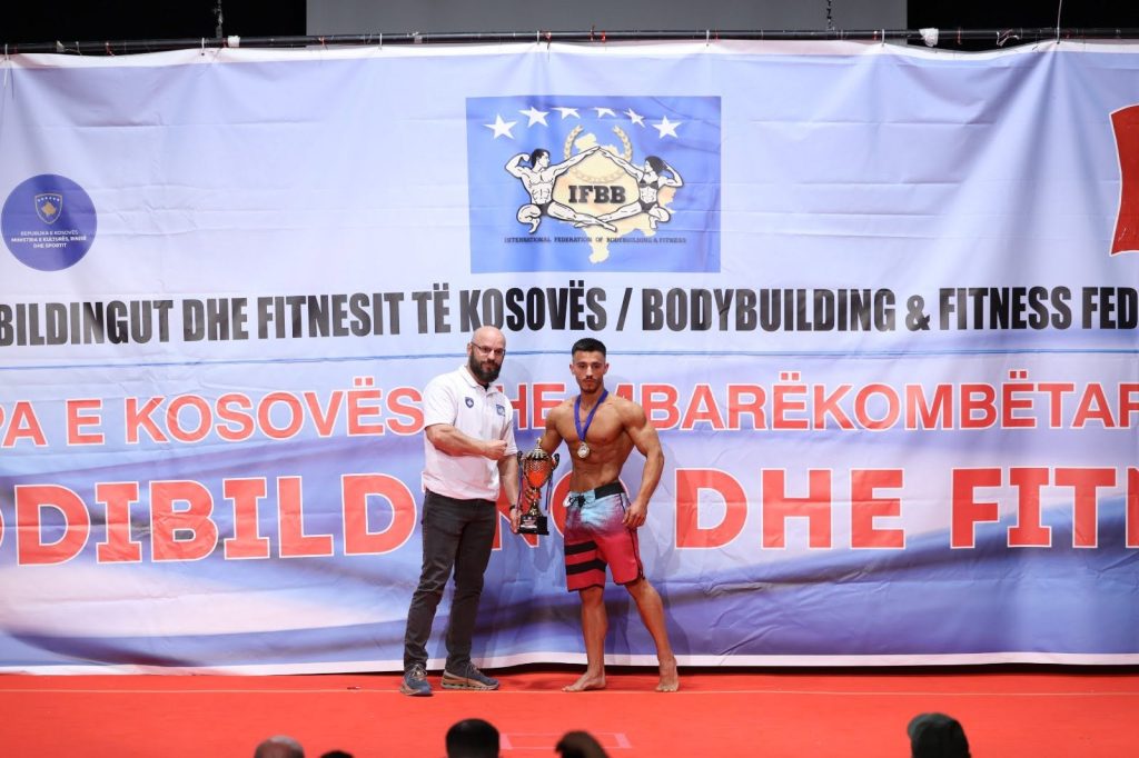 Një garues duke marrë trofeun nga një zyrtar në skenë.