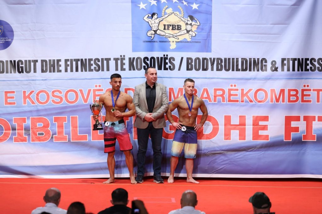 Dy garues të physique me medalje dhe një zyrtar në skenë.